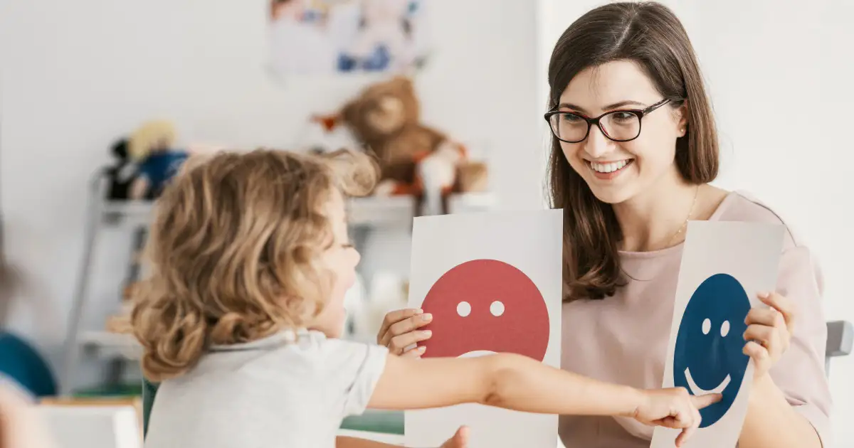 A woman holds two signs with different facial expressions while a young child points at the blue happy face.