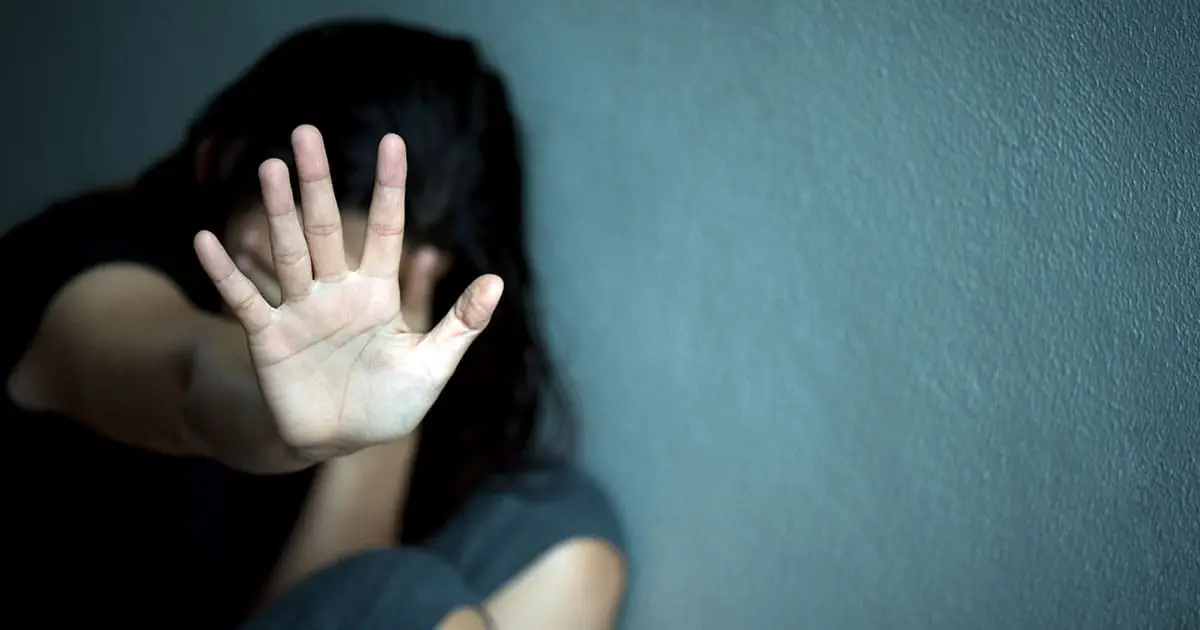 A person sits against a wall with their hand raised toward the camera, obscuring their face—a gesture often seen in those seeking support from mental health services or Choices Psychotherapy to stop or avoid overwhelming emotions.