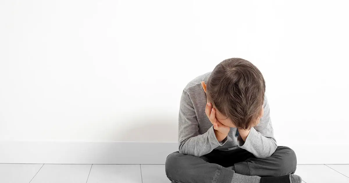 A young boy sits on the floor against a white wall with his head in his hands, appearing upset or distressed—a reminder of the importance of Choices Psychotherapy and mental health services for children in need.