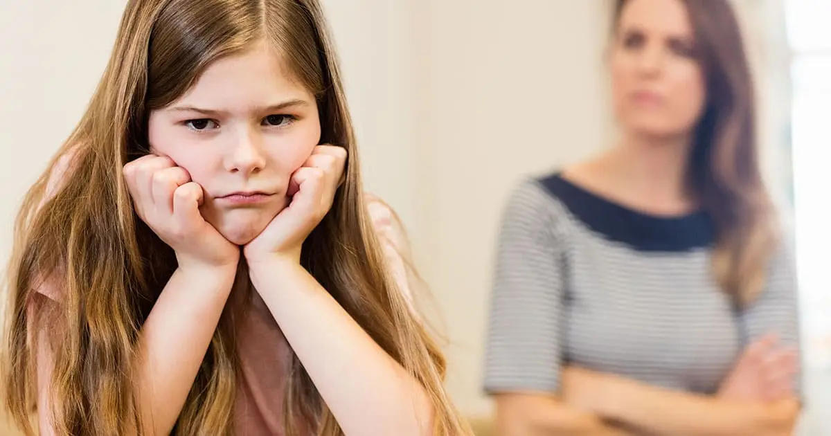A young girl with long hair rests her face in her hands and looks upset, while an adult woman stands in the blurred background with arms crossed—highlighting the importance of mental health services like Choices Psychotherapy.