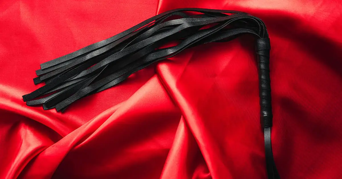 A black leather flogger with multiple tails rests on bright red satin fabric, reflecting the importance of self-awareness and seeking support like Choices Psychotherapy or other mental health services.
