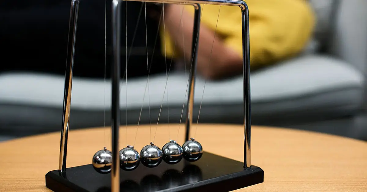A Newton's cradle with five metal balls is placed on a wooden table, symbolizing balance—reflecting the support offered by Choices Psychotherapy, with a blurred sofa and person in the background.