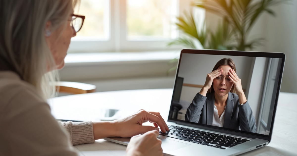 A woman on a video call sits at a desk, while another woman on the screen holds her head in apparent frustration.