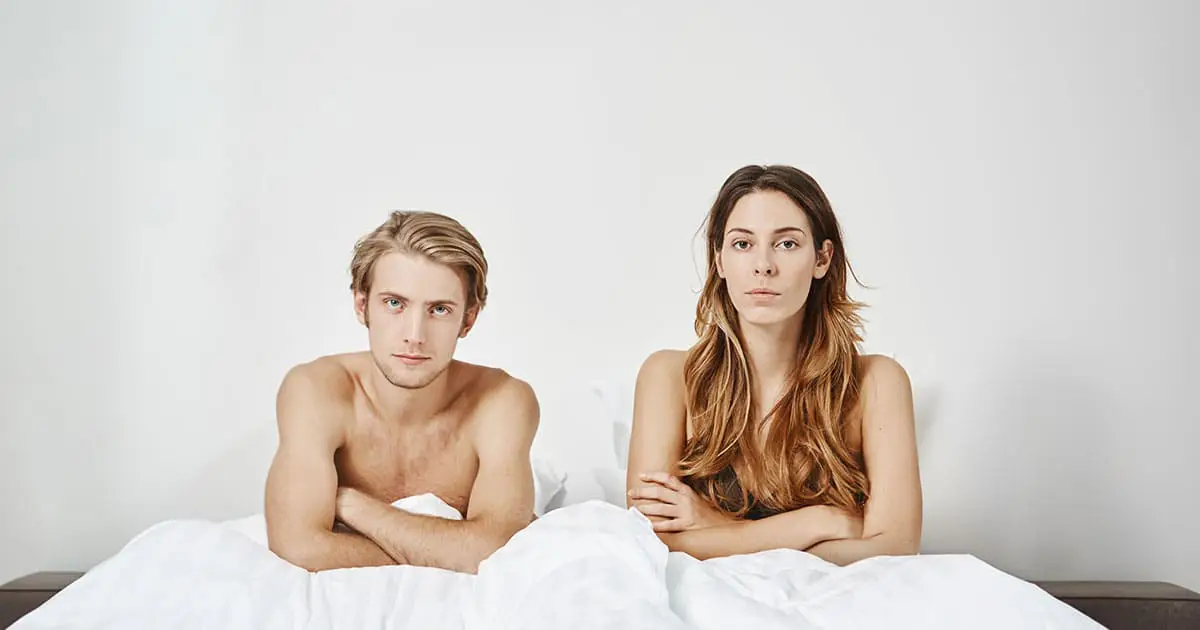 A man and a woman sit upright in bed under a white blanket, both looking straight ahead with neutral expressions—reflecting on their experiences with Choices Psychotherapy and mental health services.