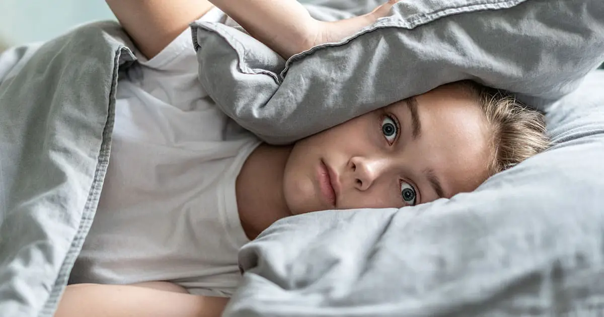 A person lies in bed, partially covered by a gray blanket, with a wide-eyed and alert expression—reflecting the struggles many face before seeking support from mental health services like Choices Psychotherapy.